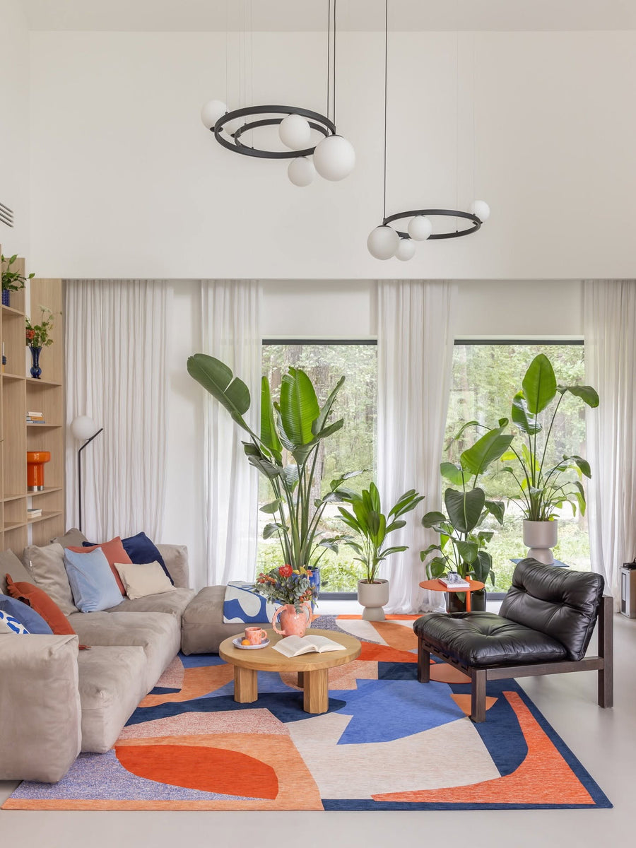 Canapé modulable Cloud en tissu beige avec coussins bleus dans un séjour lumineux, tapis graphique et grandes plantes