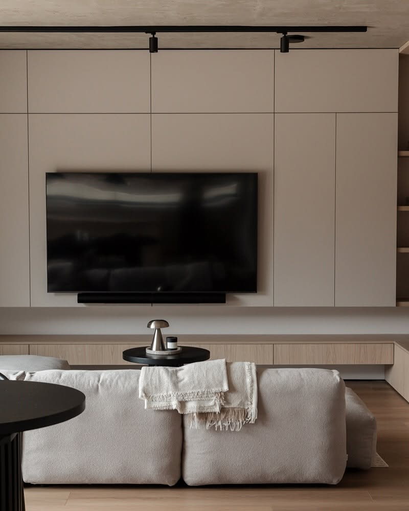 Canapé modulable Cloud en tissu beige face à un mur télé aux rangements intégrés, plaid et table d’appoint noire