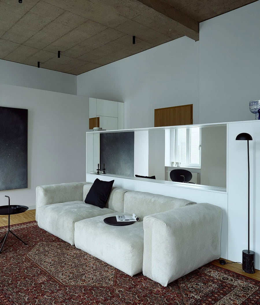 Canapé modulable Cloud en tissu blanc cassé, trois modules et pouf sur un tapis persan sous un plafond en béton brut