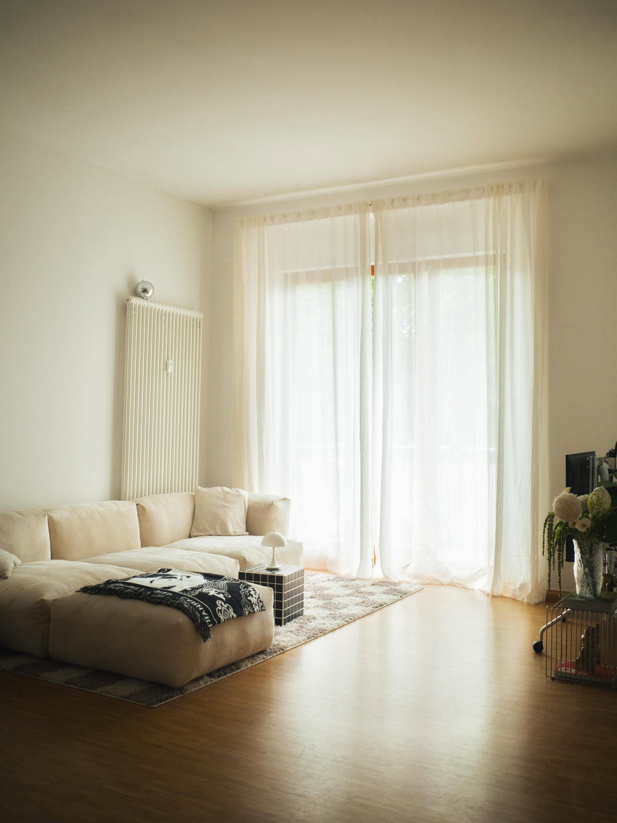 Canapé modulable Cloud en tissu écru devant une grande porte-fenêtre, plaid à motifs et lumière naturelle