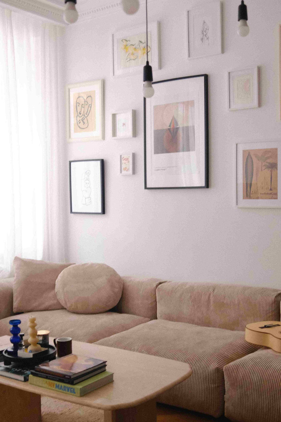 Canapé modulable Cloud en velours côtelé beige avec coussin rond, sous un mur de cadres, guitare et table basse