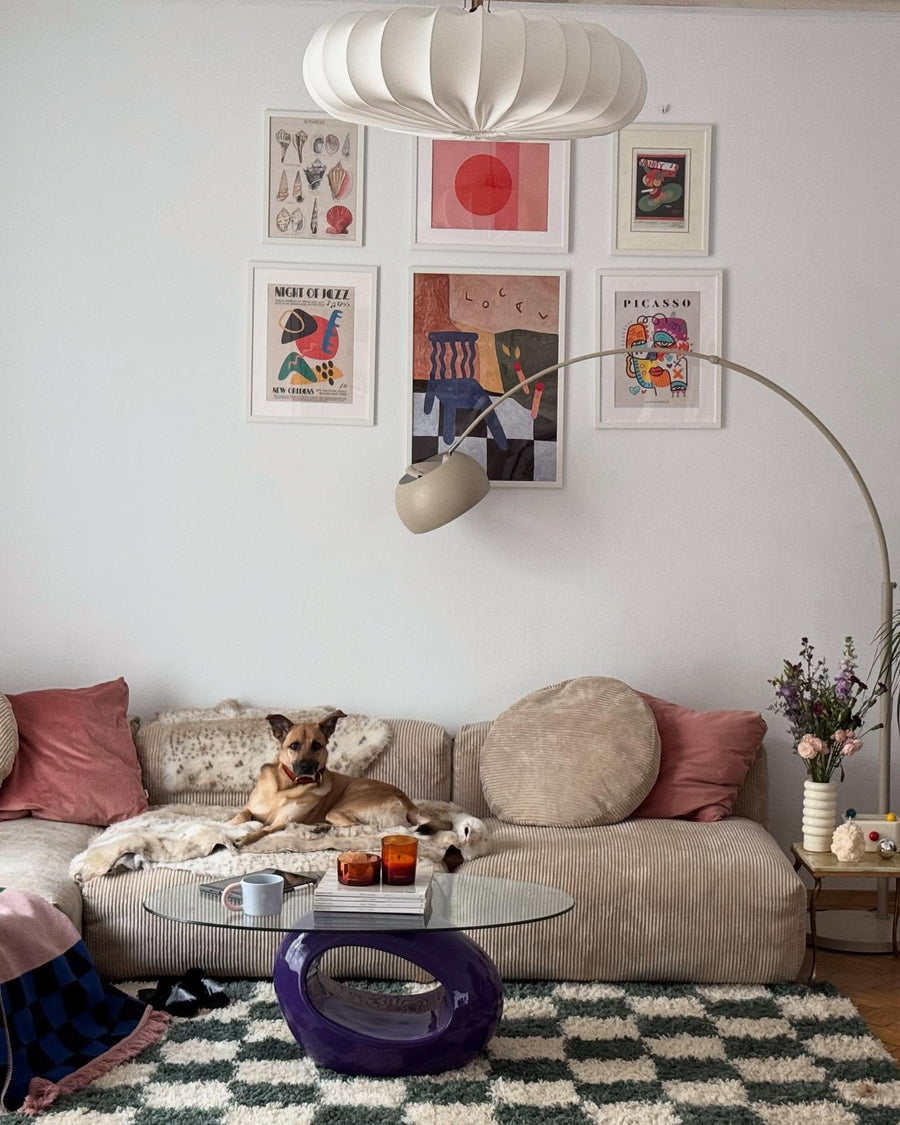Canapé modulable Cloud en velours côtelé beige dans un salon lumineux avec mur de cadres, tapis à damier et un chien allongé sur l’assise