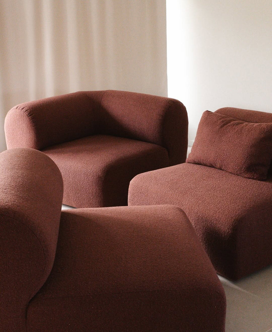 Trois modules du canapé Hug en tissu bouclé terracotta aux formes arrondies devant un rideau clair