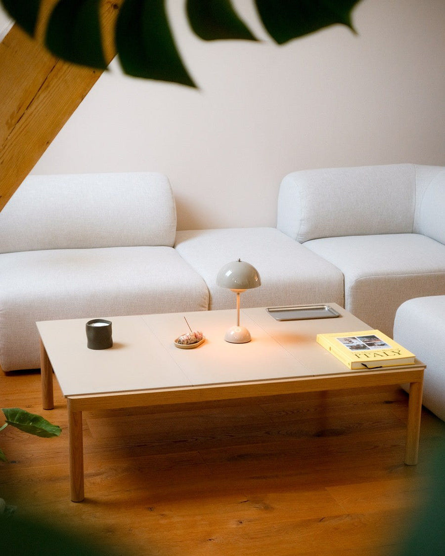 Canapé modulable Hug en tissu écru avec table basse en bois, lampe champignon et magazine, dans une pièce mansardée