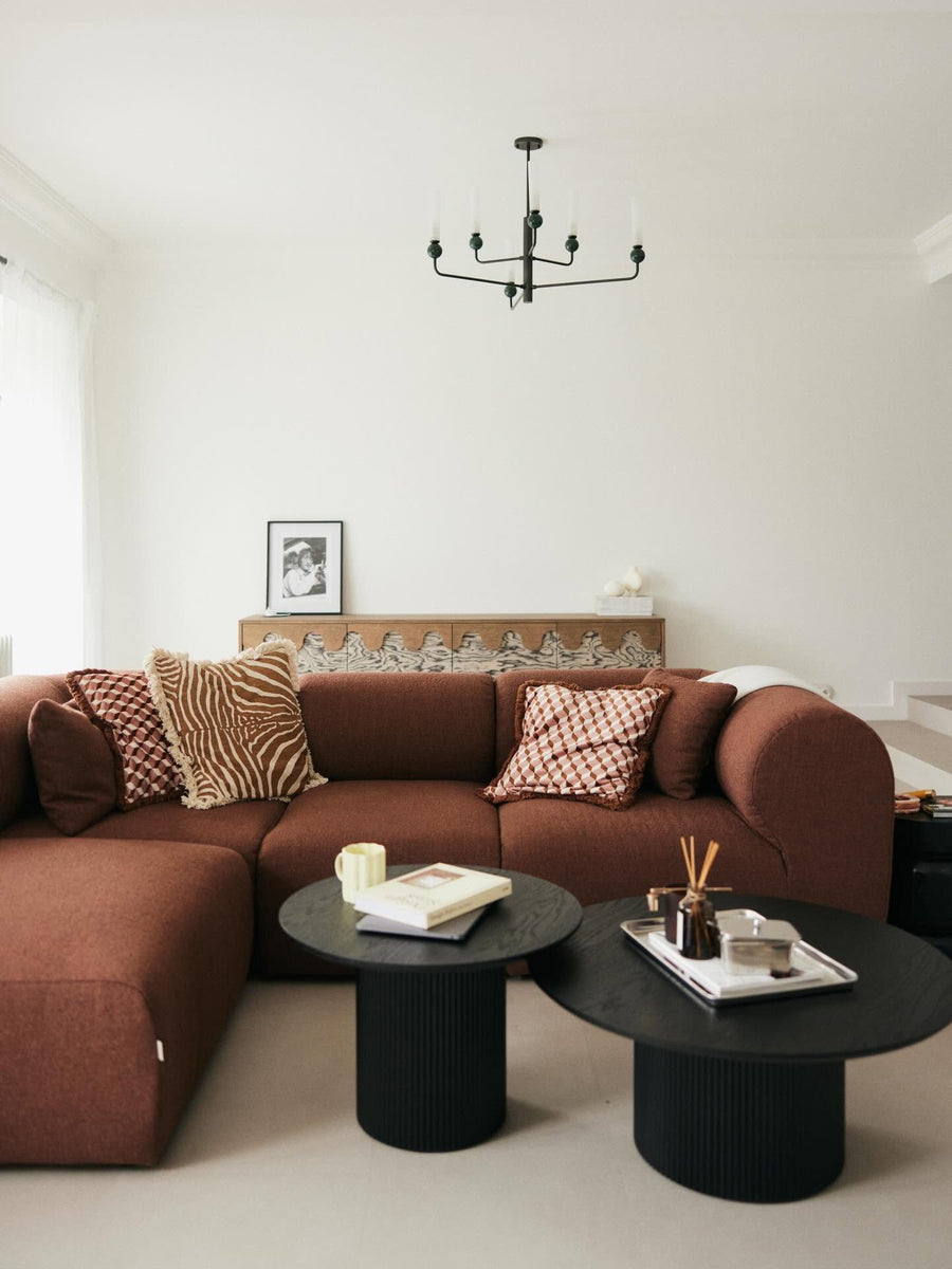 Canapé modulable Hug en tissu marron avec coussins à motifs et deux tables basses noires dans un salon blanc