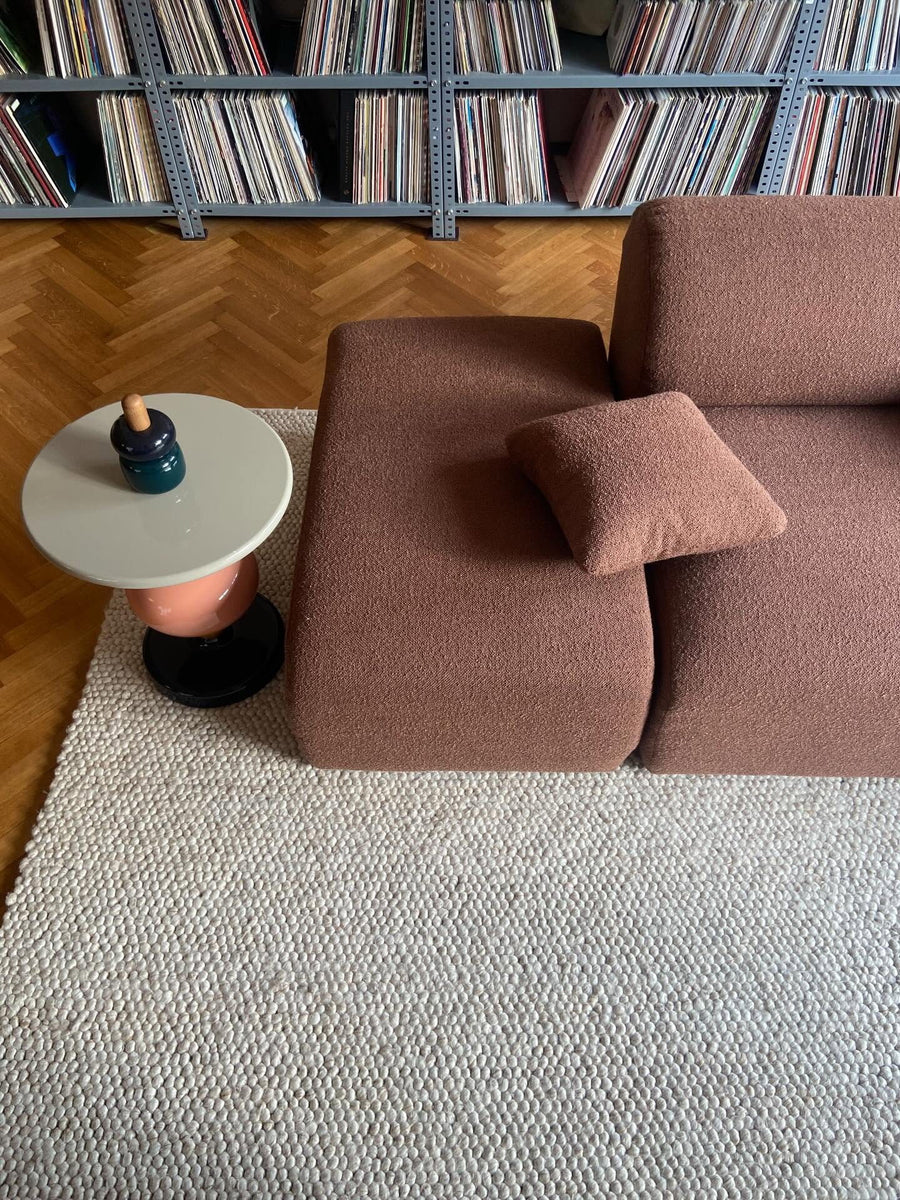 Méridienne Hug en tissu bouclé terracotta sur tapis en laine, table d’appoint ronde et mur de vinyles