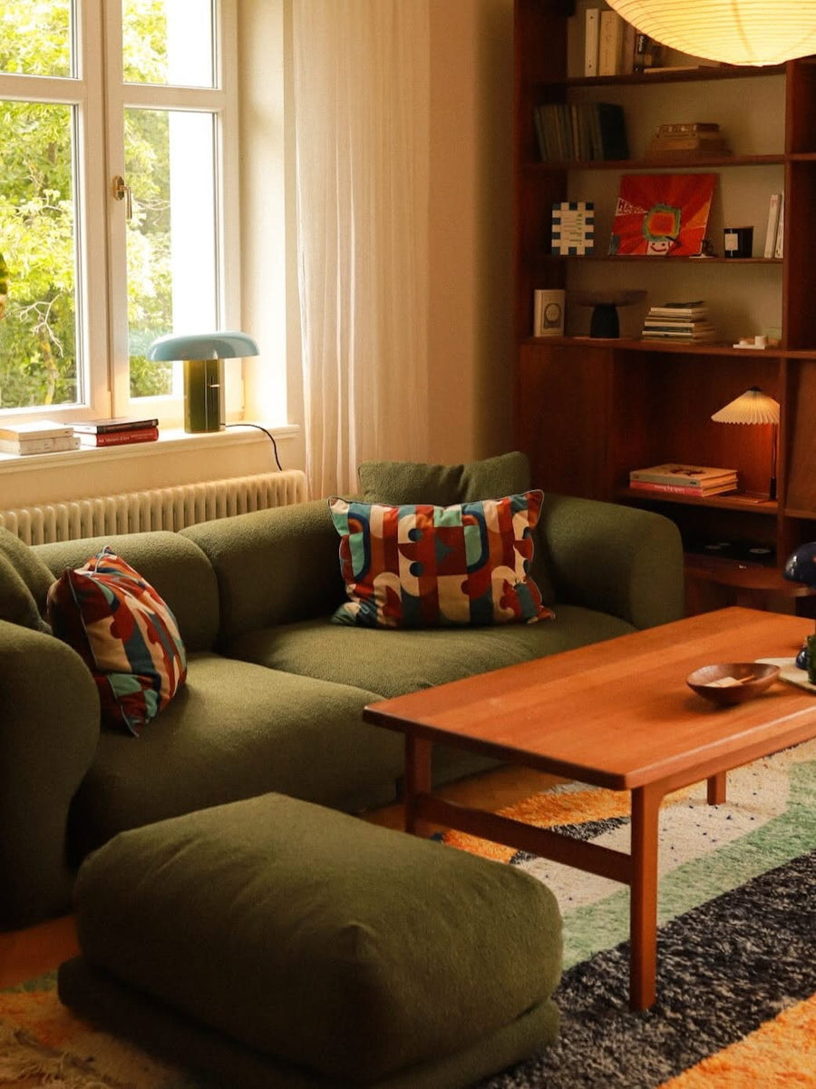 Canapé modulable Lazy en tissu vert olive avec pouf, coussins graphiques et table basse en teck sur un tapis coloré