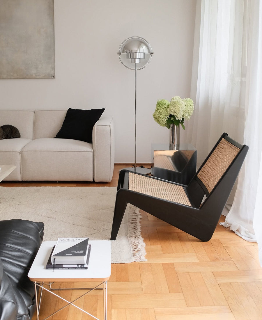 Canapé modulable Slay en tissu écru avec coussin noir, fauteuil en cannage et lampadaire chromé sur parquet en point de Hongrie
