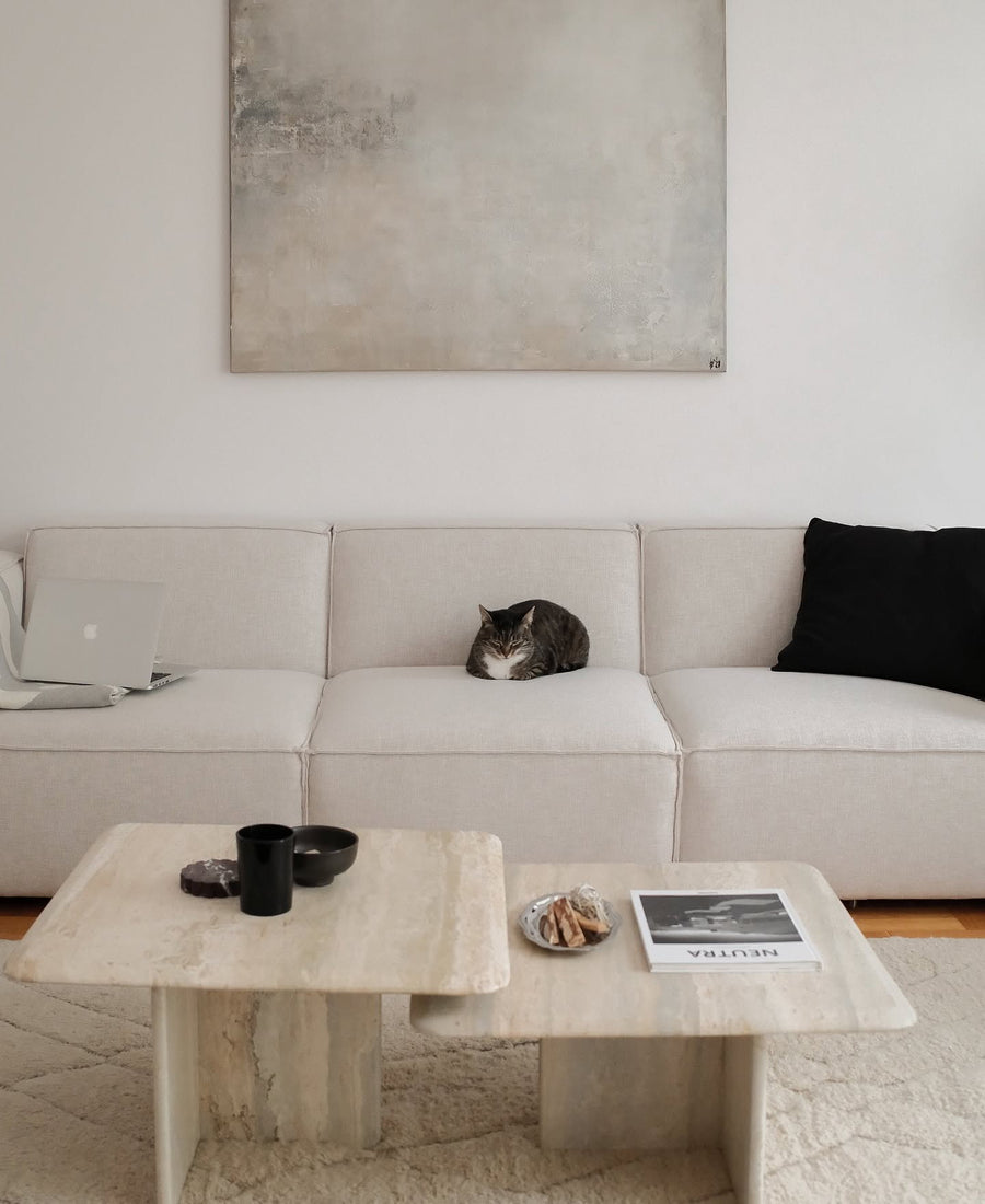 Canapé modulable Slay trois modules en tissu écru avec coussin noir, table basse en travertin et un chat endormi