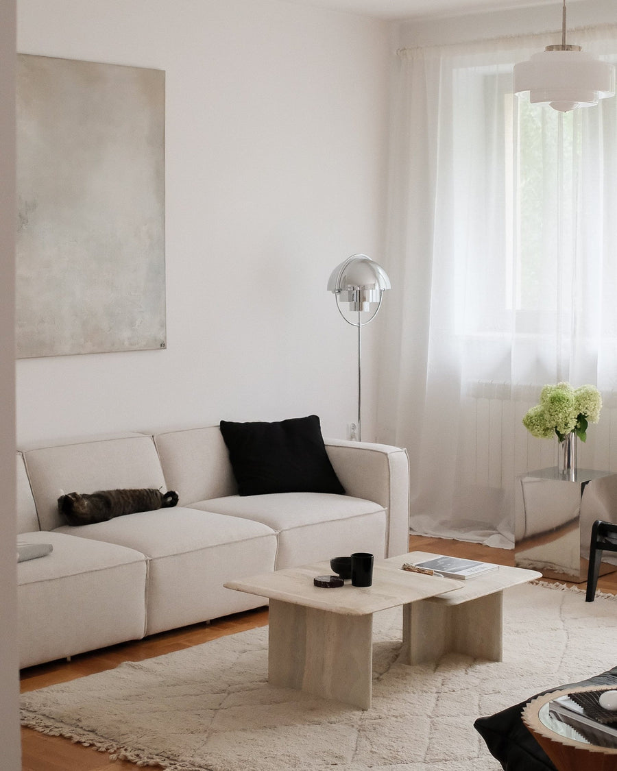 Canapé modulable Slay en tissu écru trois modules, coussin noir, table basse en travertin et lampadaire chromé