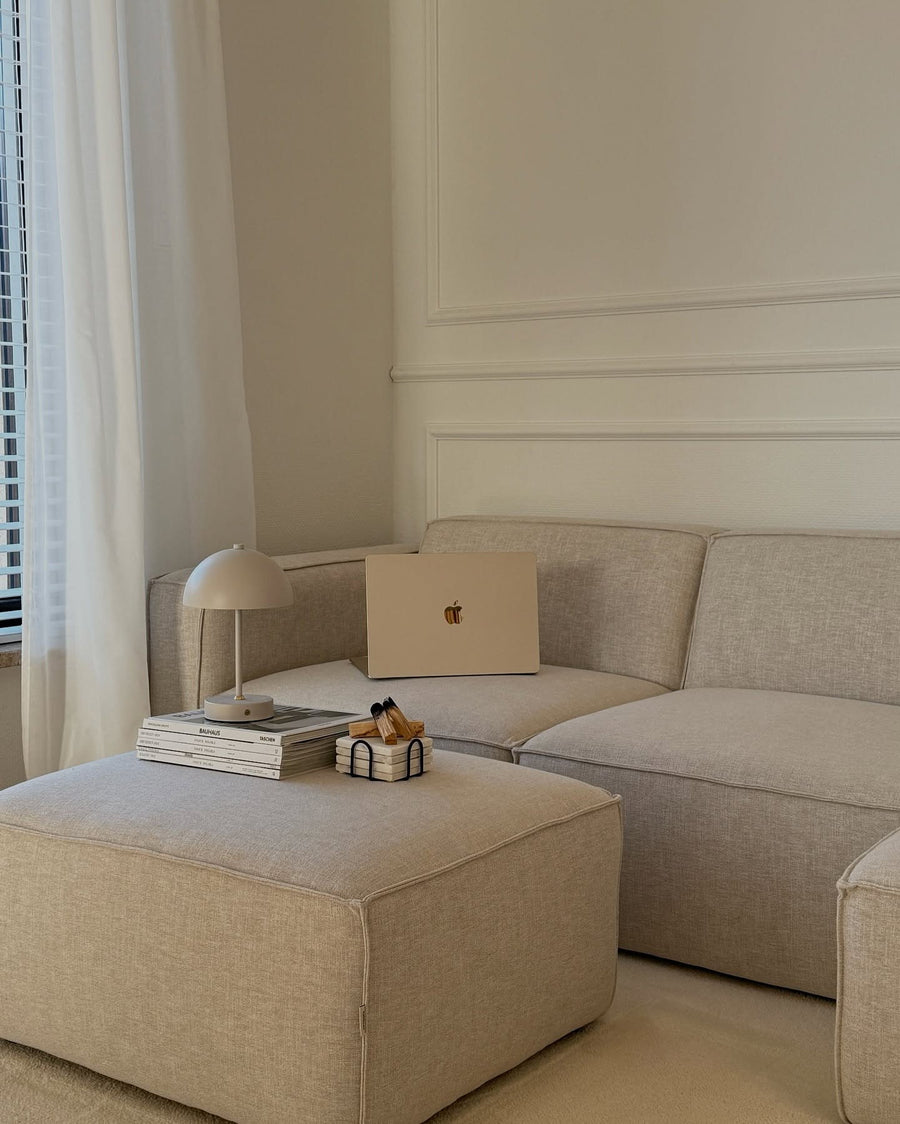 Canapé modulable Slay en tissu gris clair avec pouf, lampe et ordinateur portable dans un salon aux moulures