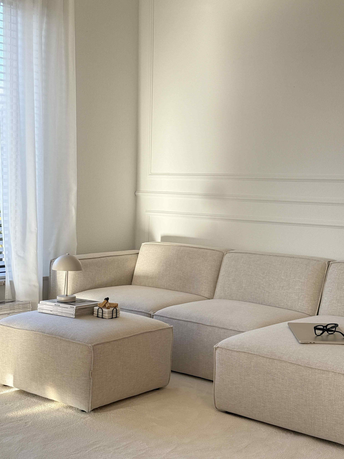 Canapé modulable Slay en tissu crème avec pouf, dans un salon aux moulures claires
