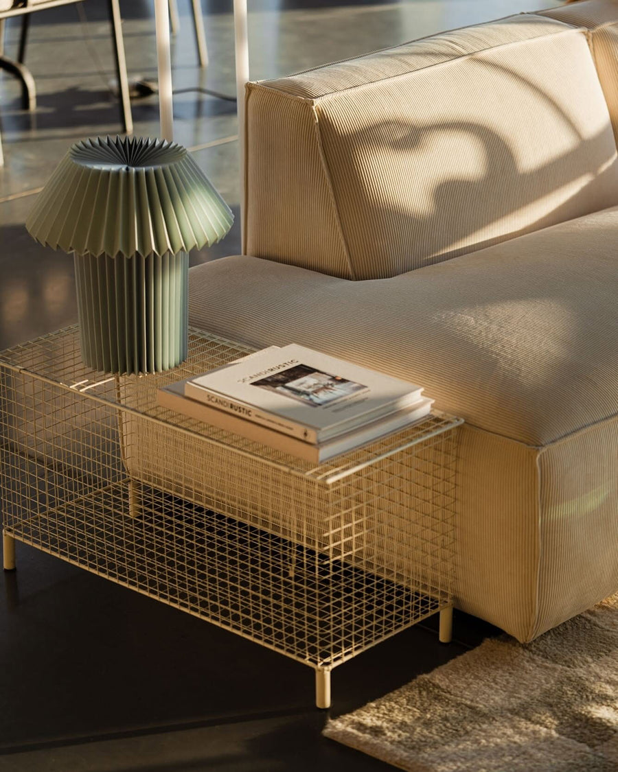 Canapé modulable Slay en velours côtelé beige dans un loft ensoleillé, table basse grillagée et lampe plissée verte