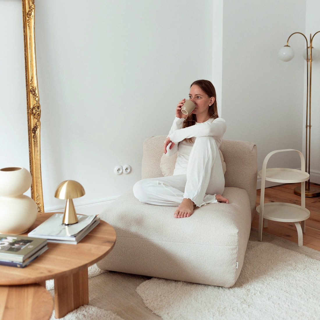 Femme relaxant sur un canapé clair avec une tasse de café, dans un intérieur lumineux et épuré.