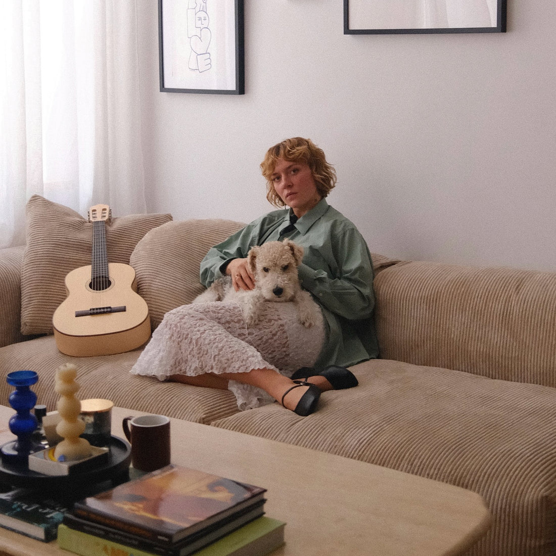 Femme assise sur un canapé beige avec son chien et une guitare, créant une ambiance chaleureuse et artistique.