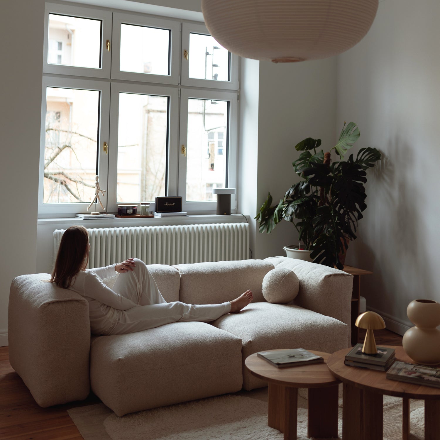 Femme assise sur le canapé modulable CLOUD en tissu crème, dans un intérieur lumineux et apaisant.